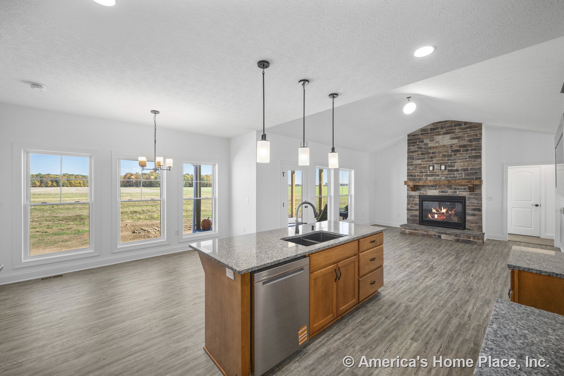 Open-concept kitchen and living area with vaulted ceiling, stone fireplace and wood mantel, granite kitchen island with sink, pendant lighting, built-in cabinetry, wood-look