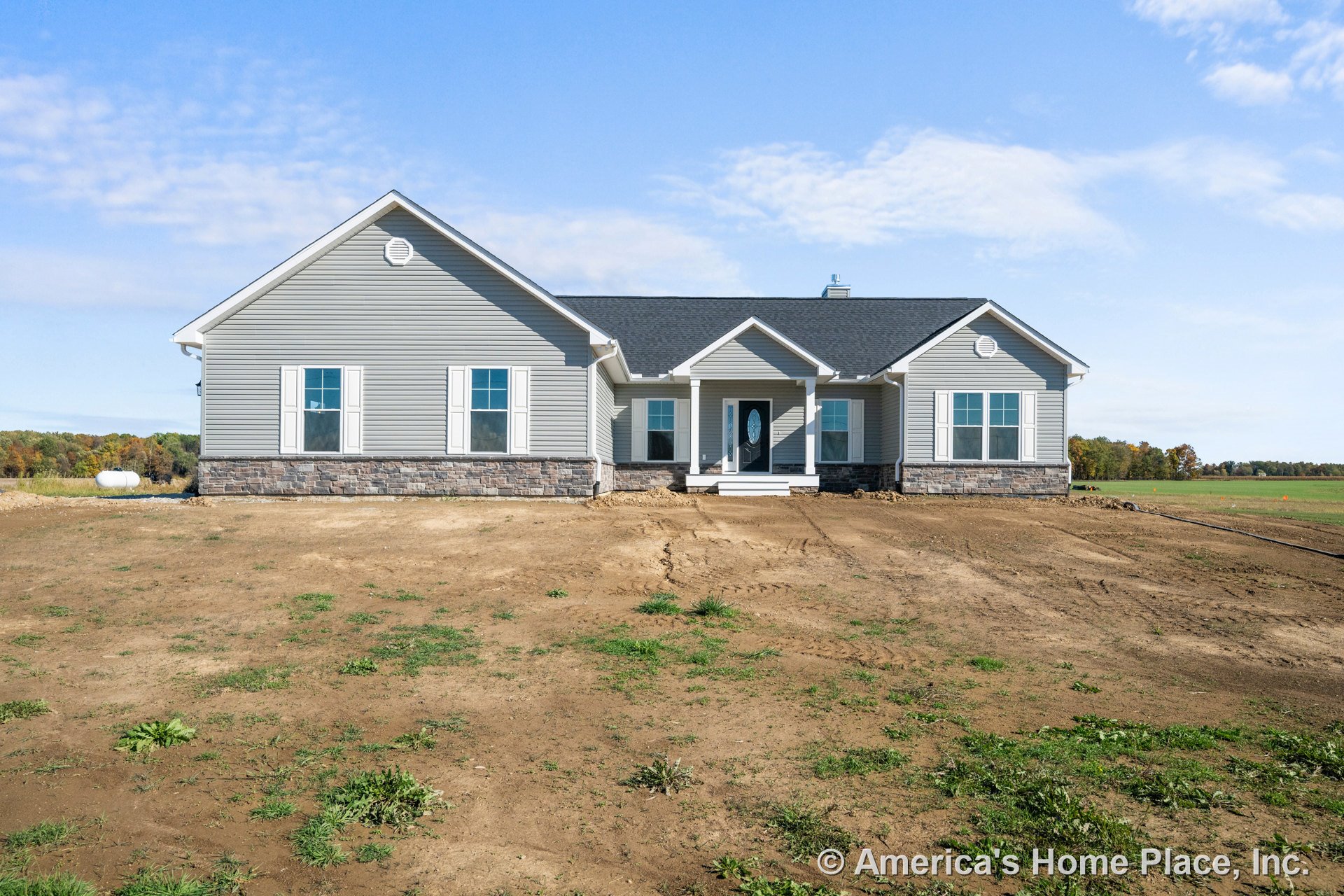 Gray vinyl siding exterior with stone veneer foundation, white trim, multiple double-hung windows with white shutters, covered front porch, oval glass front door, and gable roof in