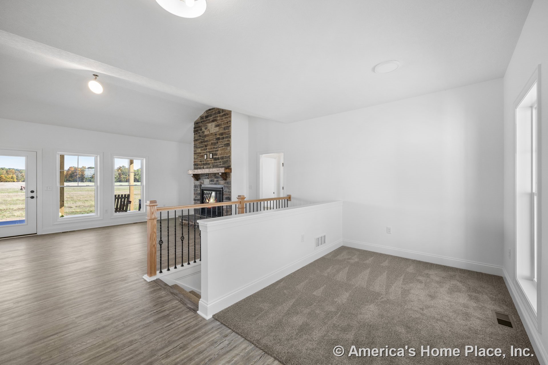 Brick fireplace with wood mantel, three large windows, glass exterior door, carpeted stair landing, wood-look vinyl flooring, white trim and walls, open living room layout, ceiling