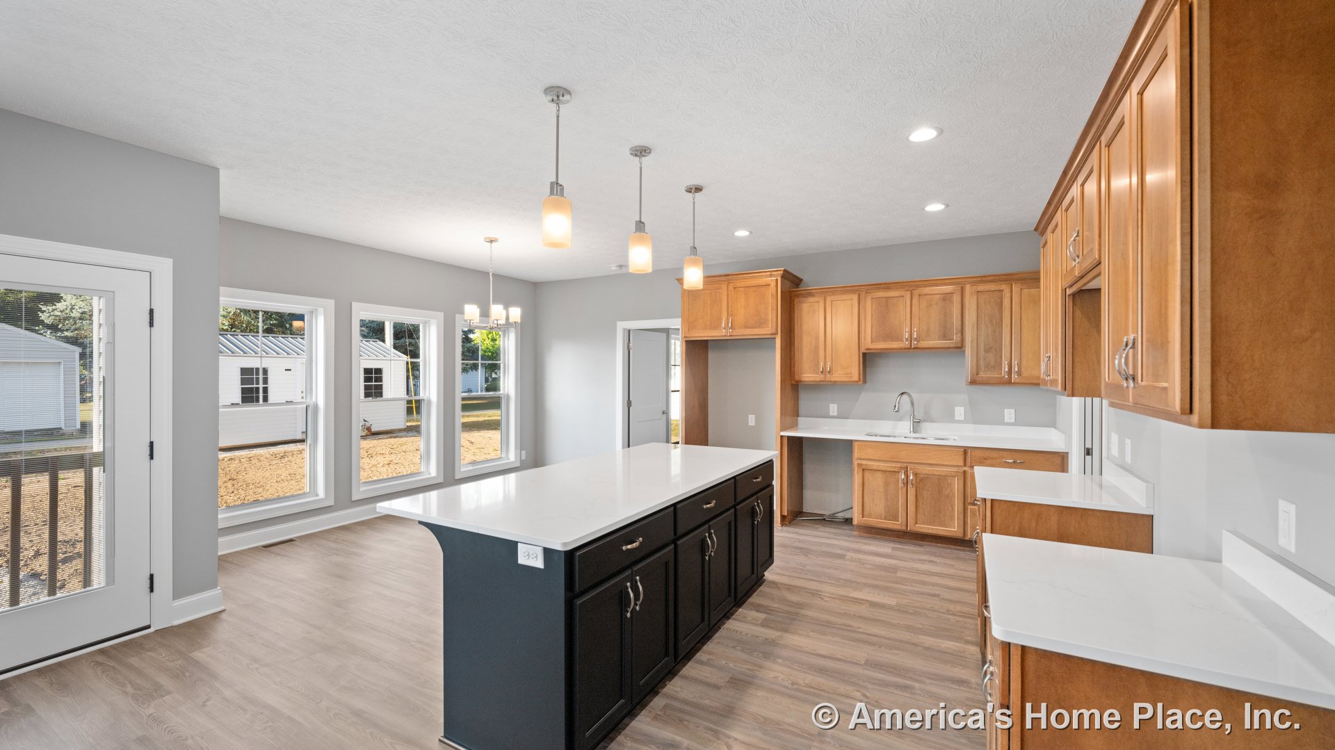 Wood cabinetry with brushed metal handles, white quartz countertops, large central island with built-in sink, three pendant lights above island, wide plank wood-look flooring