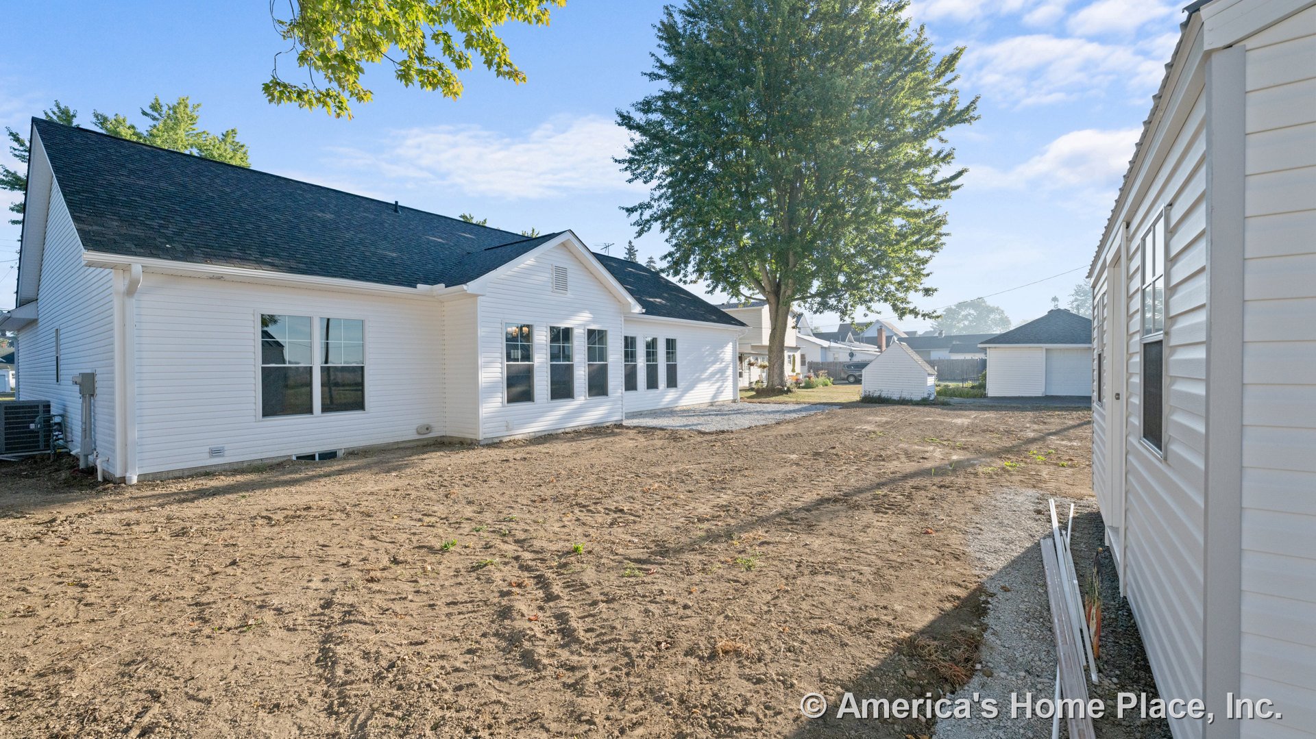 White brick single-story home with black shingle roof, multiple large windows, ground-level foundation, vinyl-sided outbuilding, and gravel walkway in the yard.