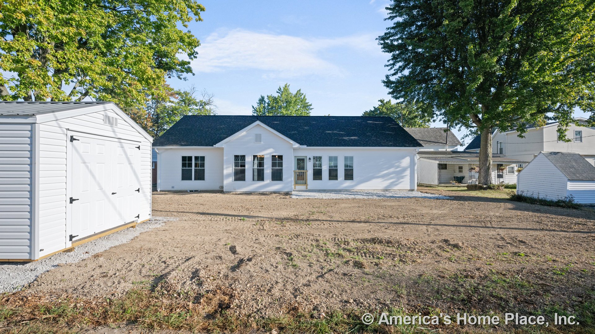 White single-story home with black shingle roof, multiple front windows, covered entry porch, detached garage, and unfinished front yard.