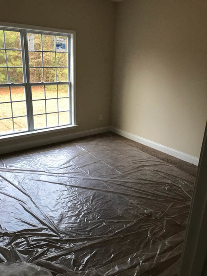 White-walled room with plastic sheeting covering the floor, single window featuring a taped sign, recessed ceiling light, and unfinished surfaces.