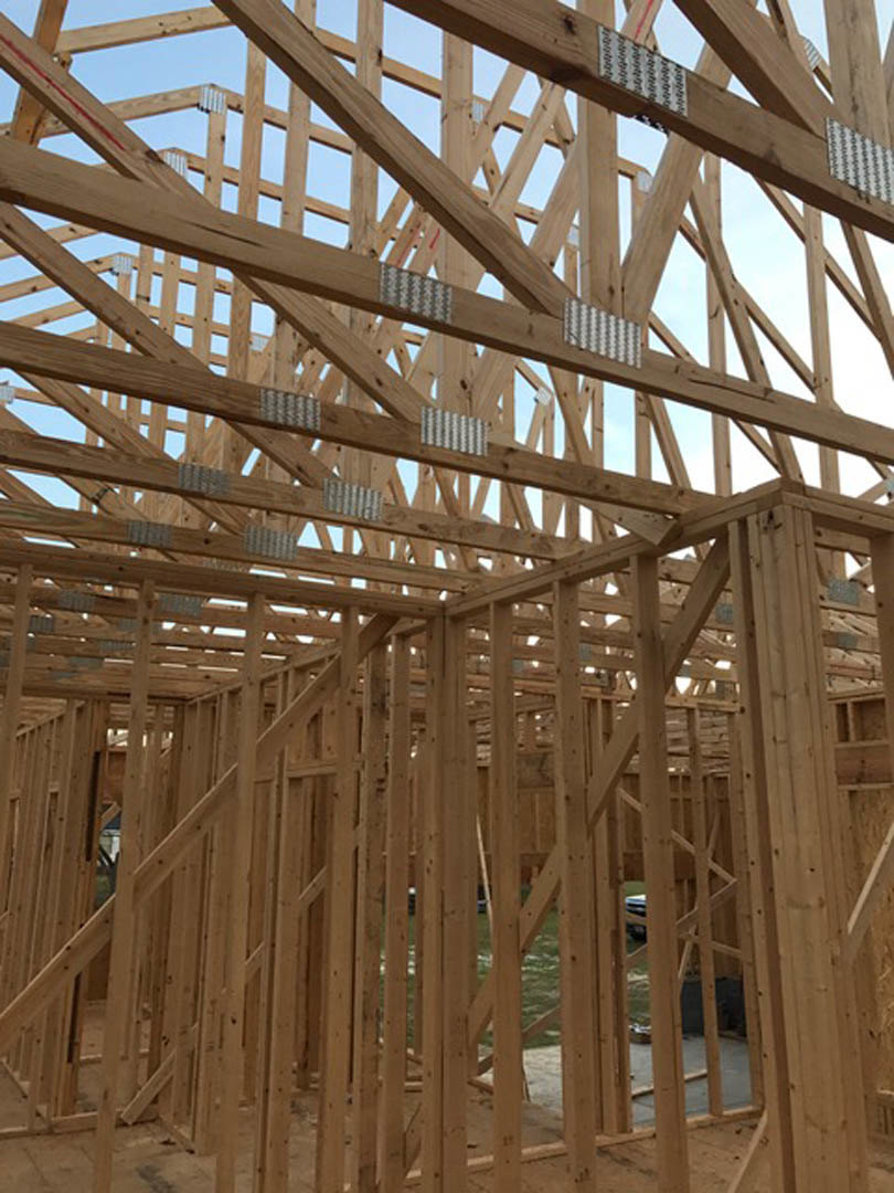 Wood-framed house under construction with exposed beams and metal studs against a clear sky