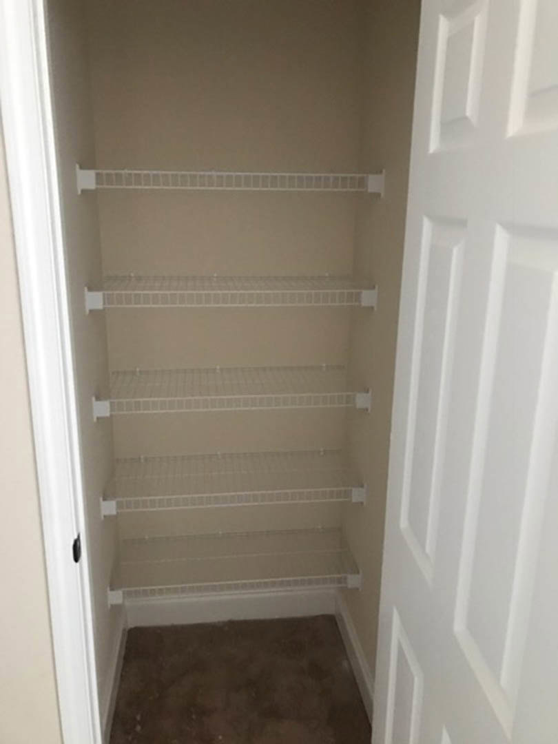 Walk-in closet with white built-in shelves, brown carpet flooring, and white plaster walls with crown molding