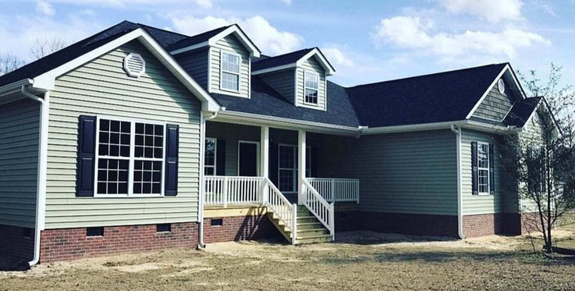 Two-story home with gray siding, white trim, covered front porch with white railings and stairs, manicured lawn, large windows, tree in the background, and white roof vent.