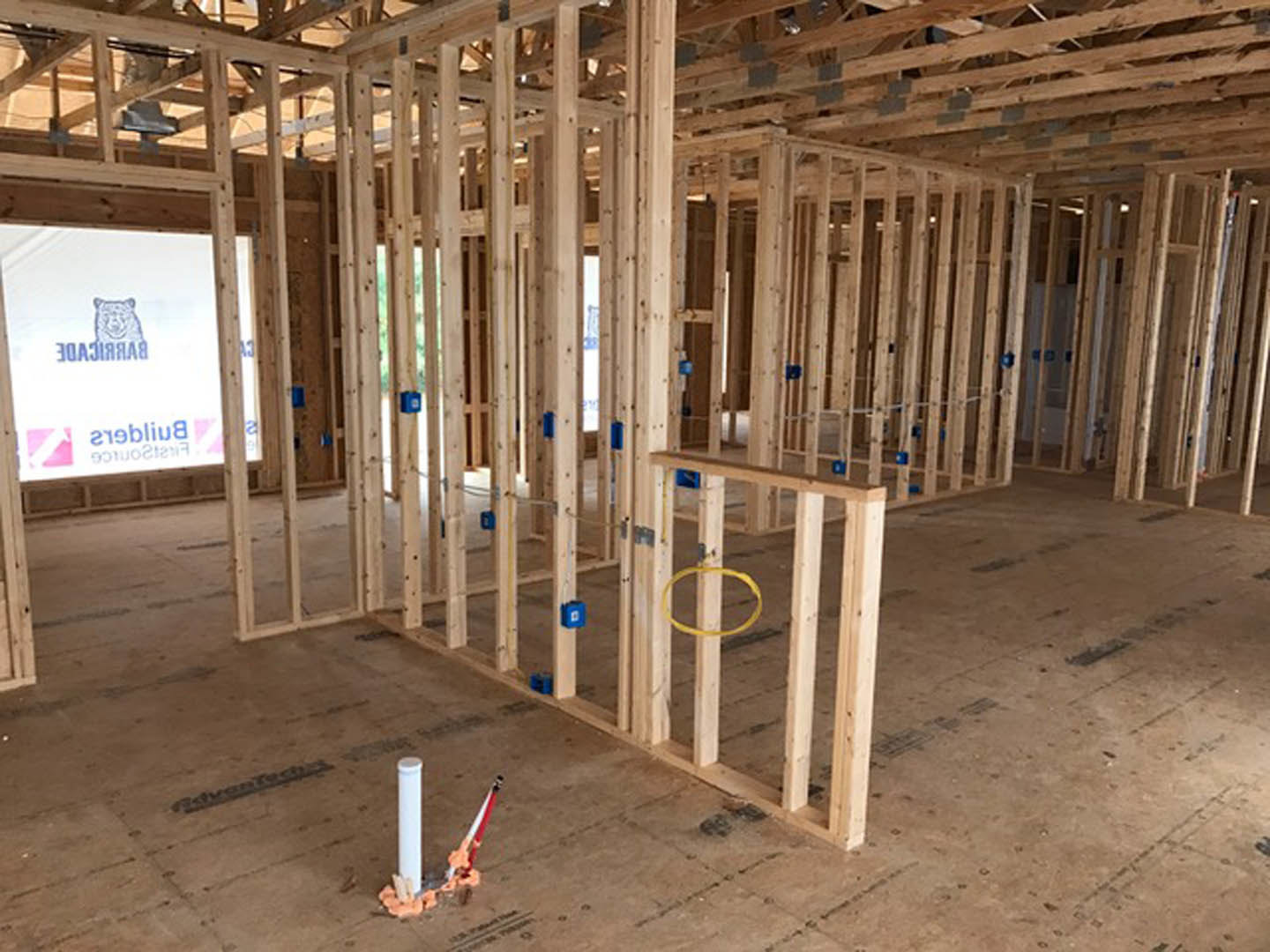 Exposed wood beams and unfinished lumber frame a spacious interior under construction, with visible ceiling joists and subfloor.