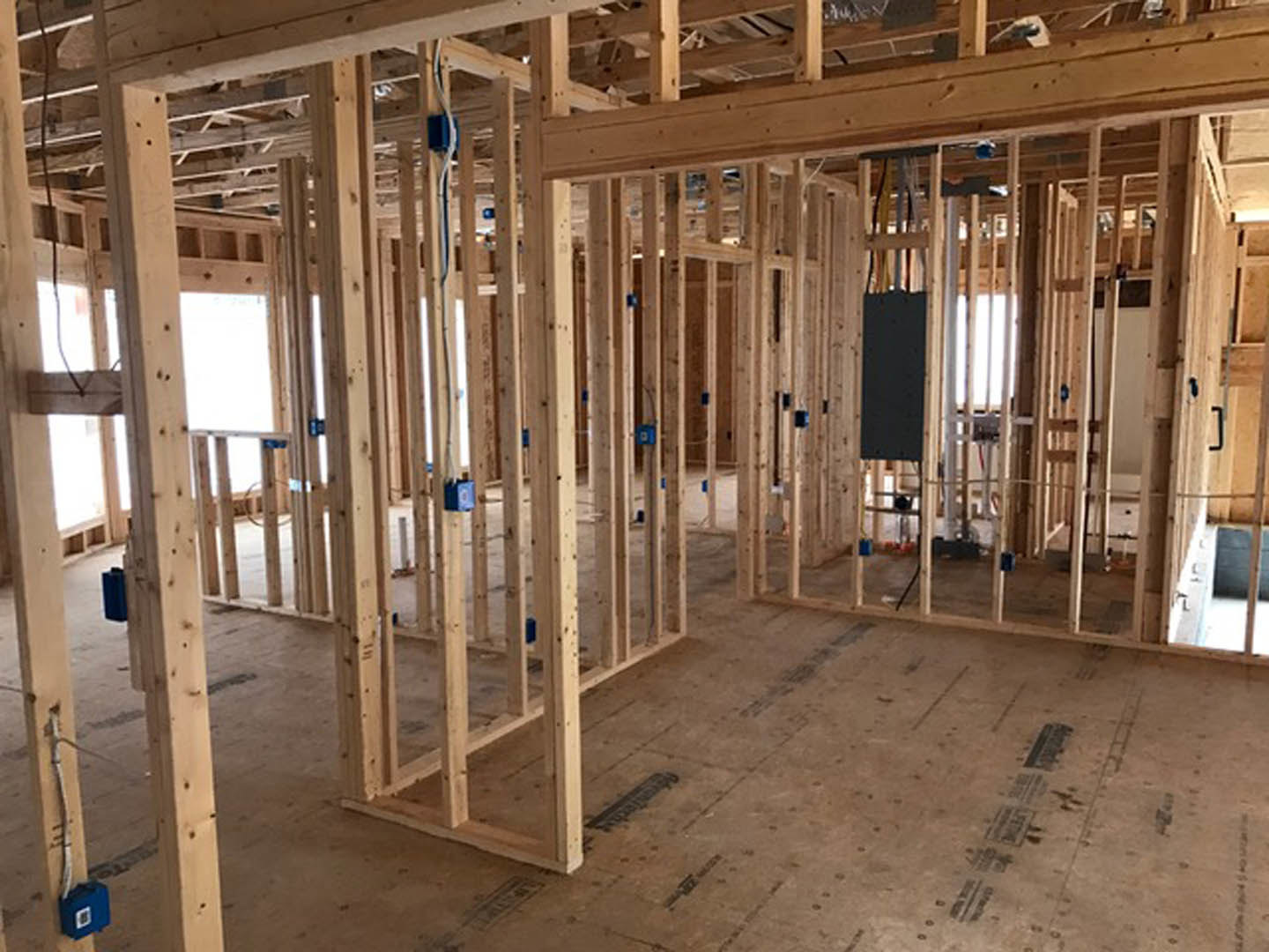 Wood-framed room under construction with exposed beams, unfinished plank flooring, and a black rectangular object resting on the floor