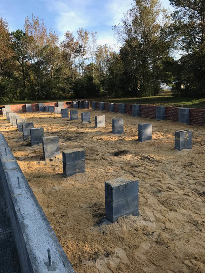 Stacked concrete blocks on sandy ground with grassy field and scattered trees in background under cloudy sky