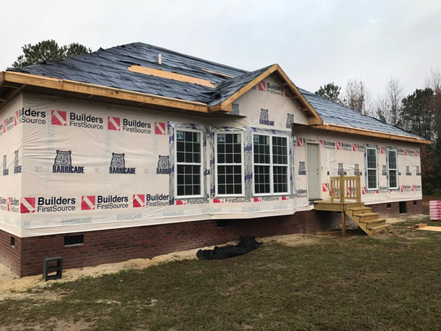 Two-story home with gray siding, white trim, covered front porch, shingle roof, and large multi-pane windows surrounded by mature trees