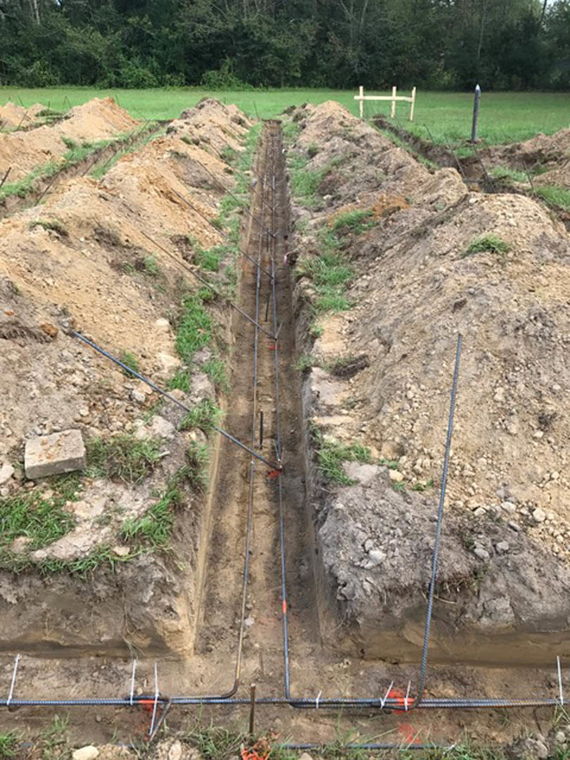 Open trench in grassy yard with exposed electrical wires, surrounded by soil and trees