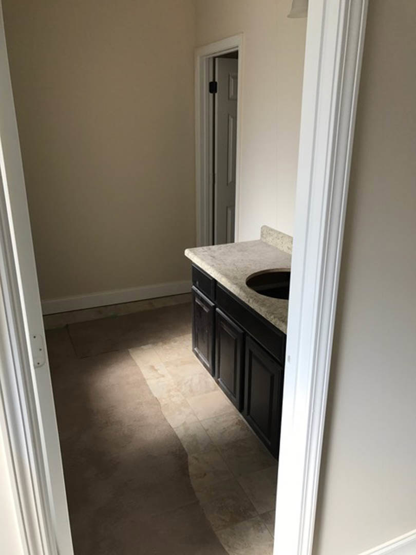 Bathroom with white ceramic sink, chrome faucet, light-colored tile flooring, wooden door, and neutral painted walls