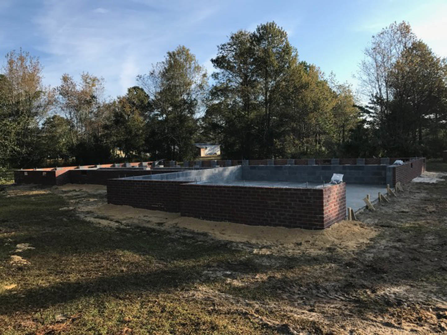 Brick exterior wall and foundation with patches of snow and grass in the foreground, leafless trees and blue sky in the background
