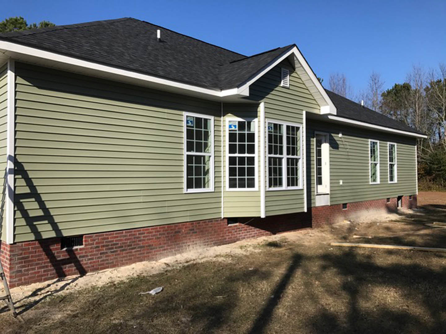 Brick facade and green siding exterior with multi-pane windows, white door, and porch under gabled roof.