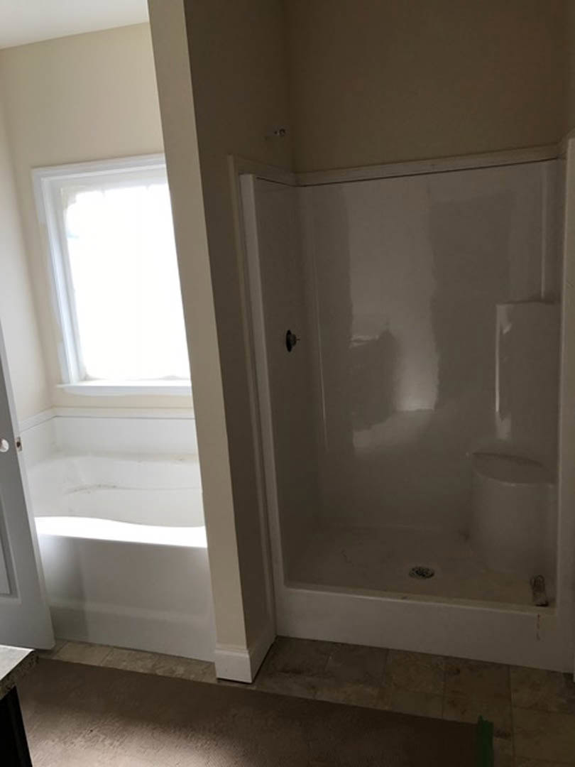 White tile shower with glass door beside a freestanding bathtub, bathroom features plaster walls, window, and modern fixtures.