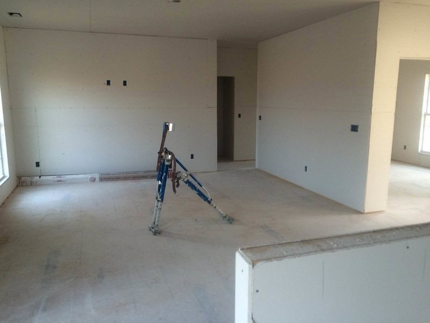 Blue and white crane positioned in a room with white plaster walls, composite flooring, ceiling fixture, and window.