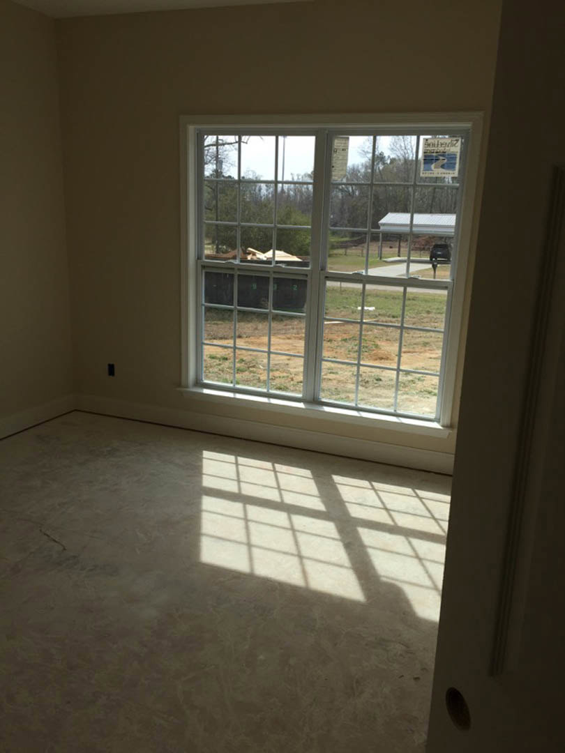 Sunlit room with hardwood flooring, large window overlooking grassy yard and trees, window blind partially drawn, wall painted light neutral color