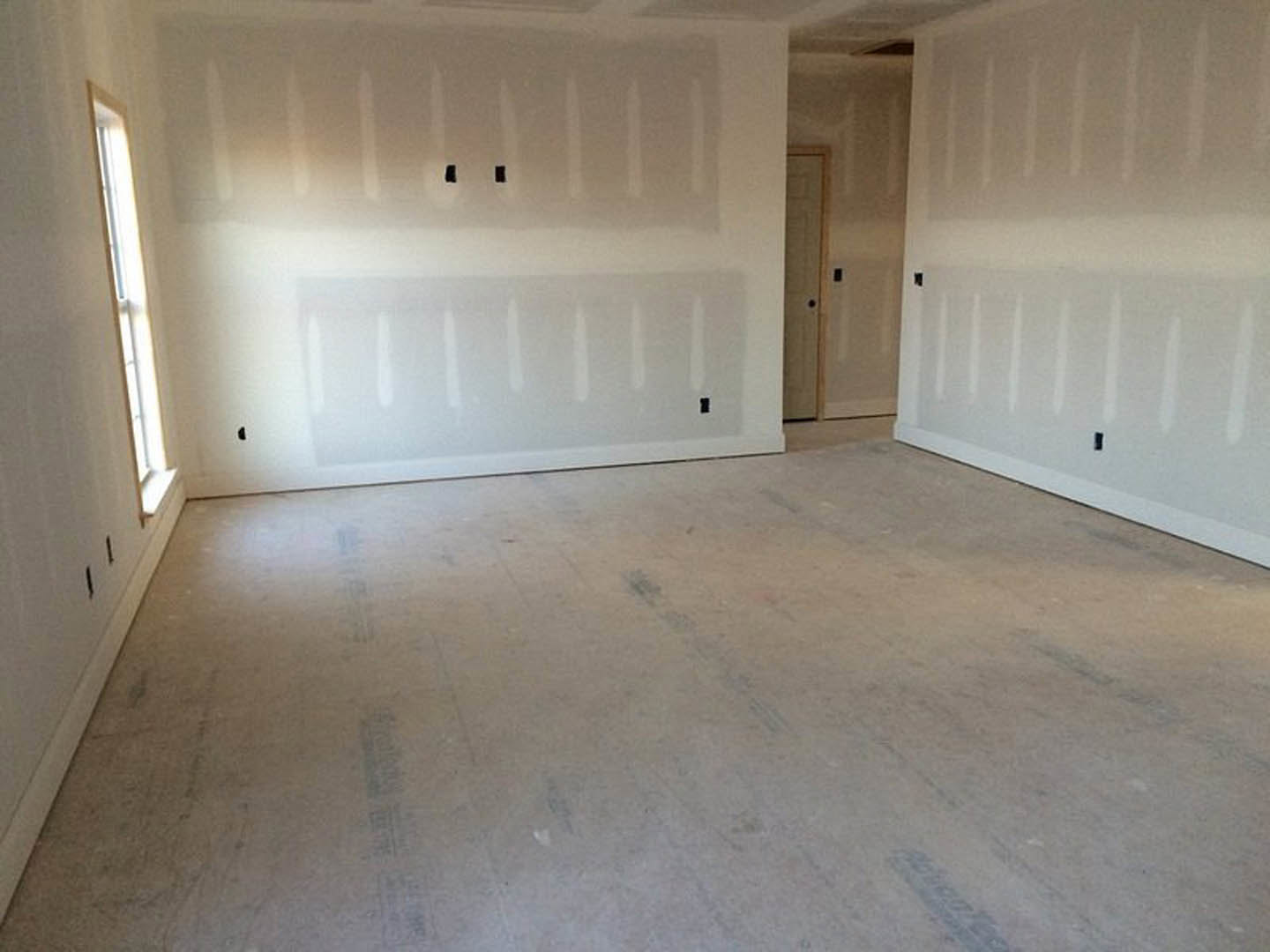 White-walled room with a window, white floor showing black marks, wall with visible holes, partially visible door, and white paint finish.