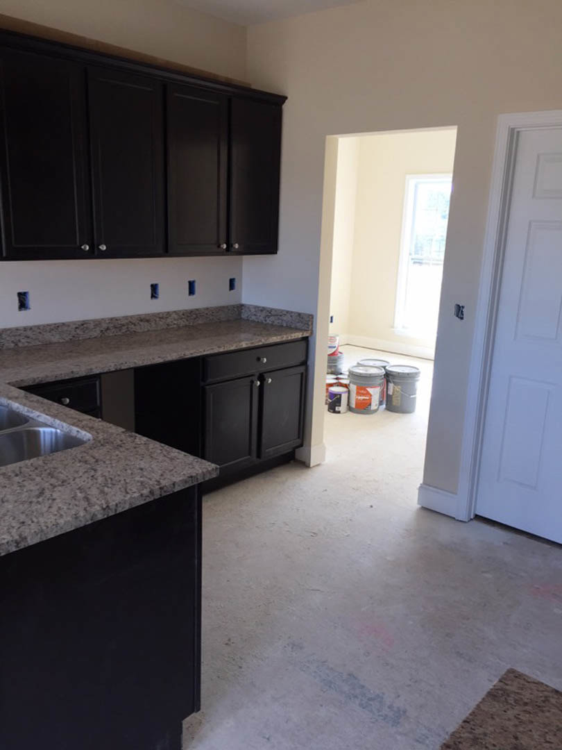 Granite countertops with undermount sink, black cabinets with silver knobs, white door, paint buckets on tile floor, close-up of sink and grey bucket with white lid