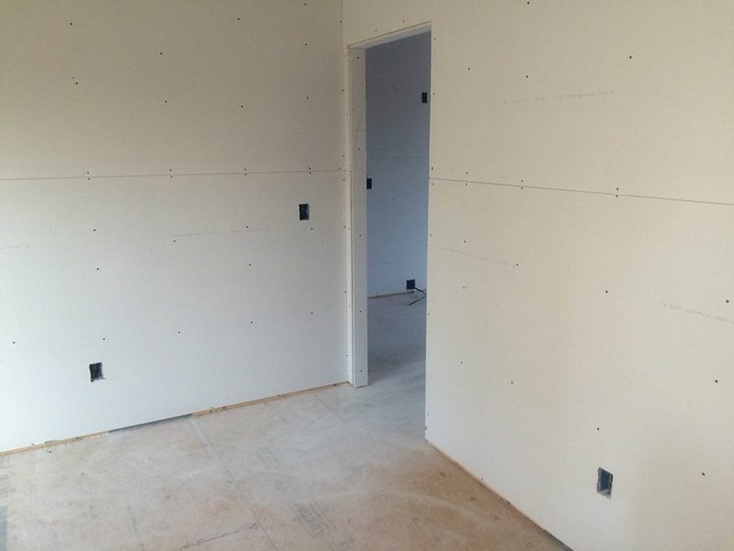 White plaster wall with a rectangular hole, open white door, tile flooring, and visible ceiling.