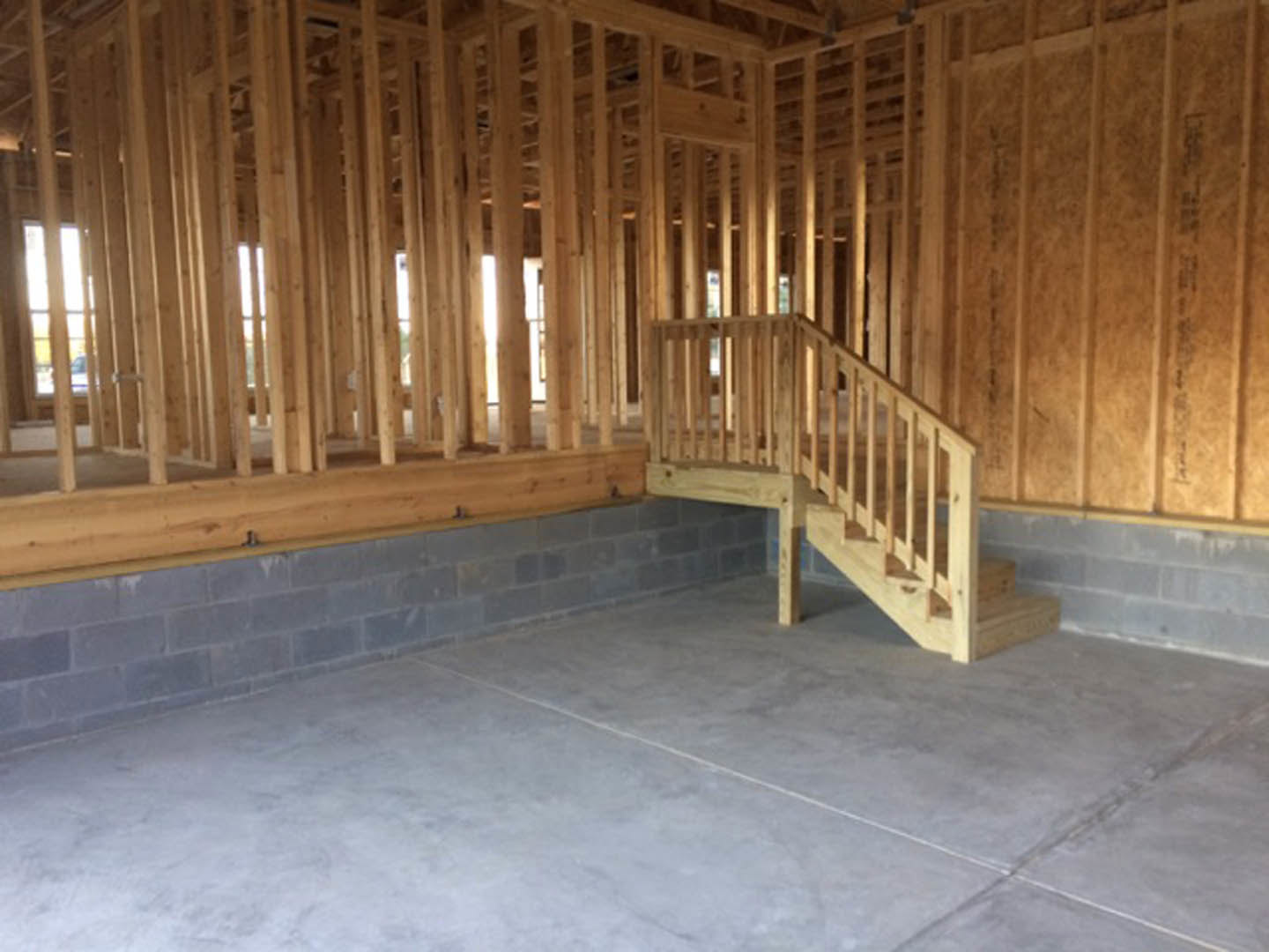 Wooden staircase with hardwood treads and risers, adjacent to a concrete floor and wooden table, framed by exposed wood beams and planks on walls.