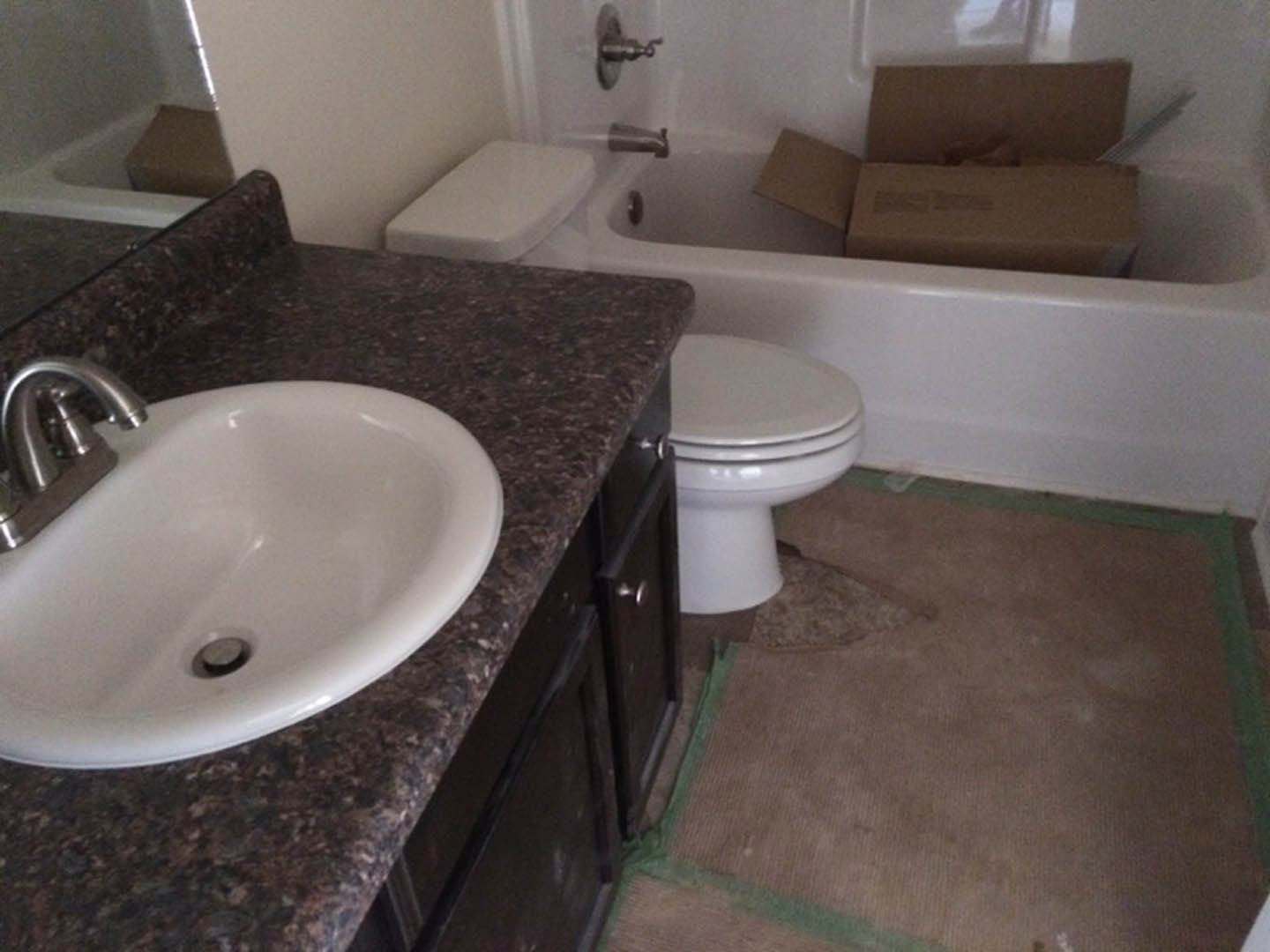 Bathroom with white tile floor, white toilet with closed lid, built-in bathtub, white sink with chrome faucet, visible drain, and neutral wall finishes.