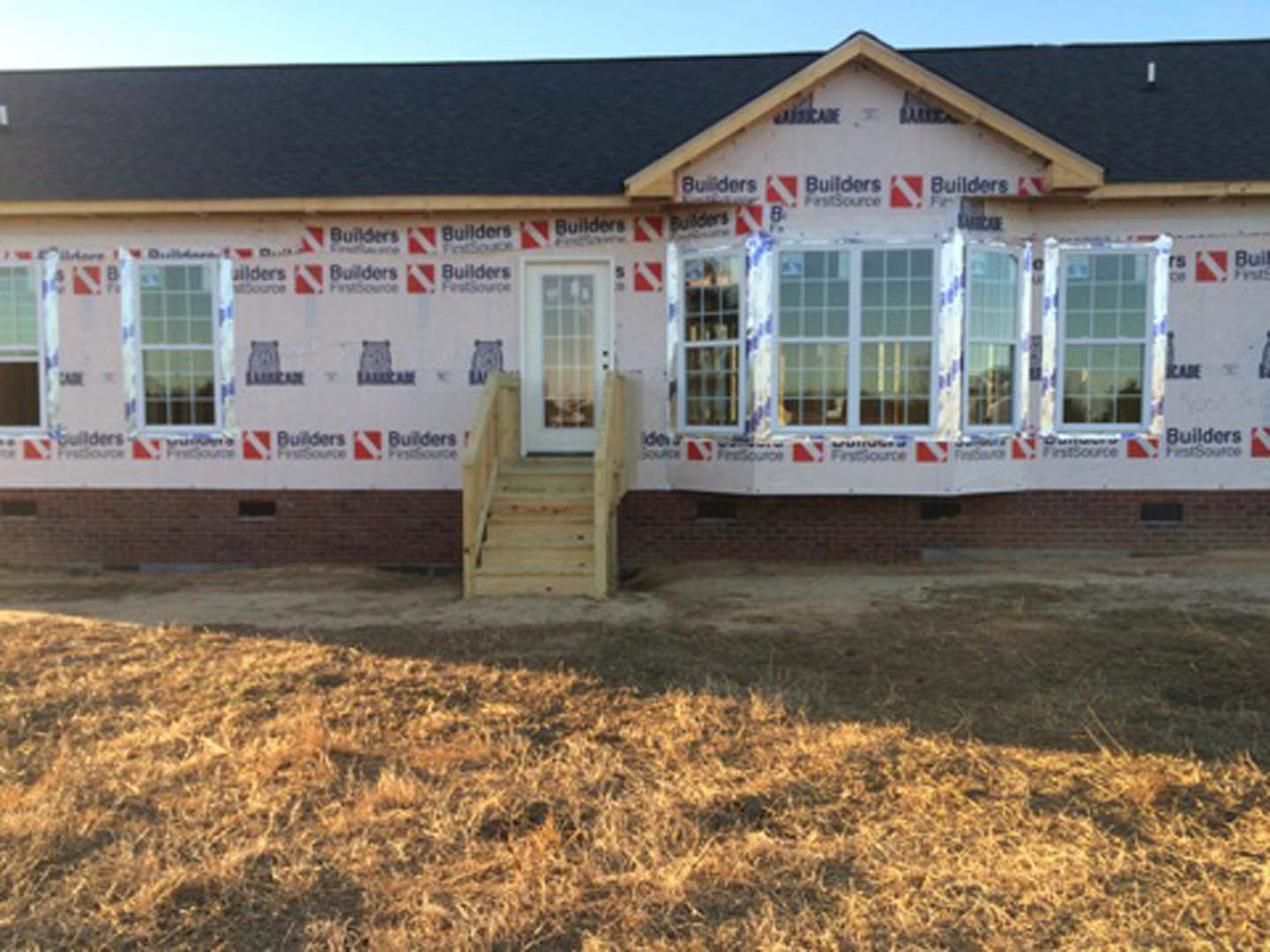 Auburn exterior with front porch, wooden stairs leading to entry door, few windows, grassy lawn, and building visible in background