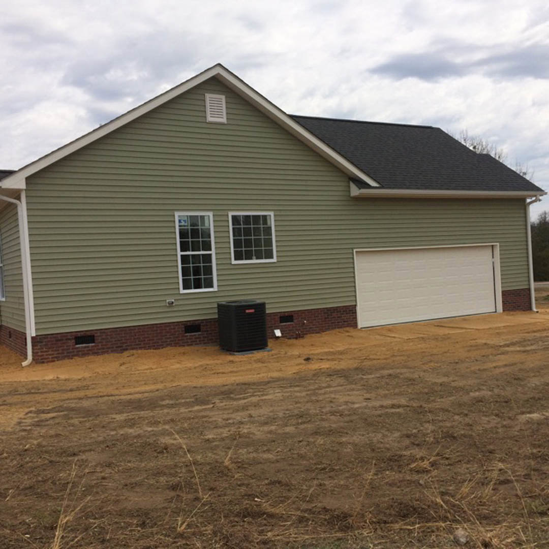 Two-story house with white siding, attached single-car garage featuring a white paneled door, rectangular windows, and a dirt driveway; cloudy sky overhead.