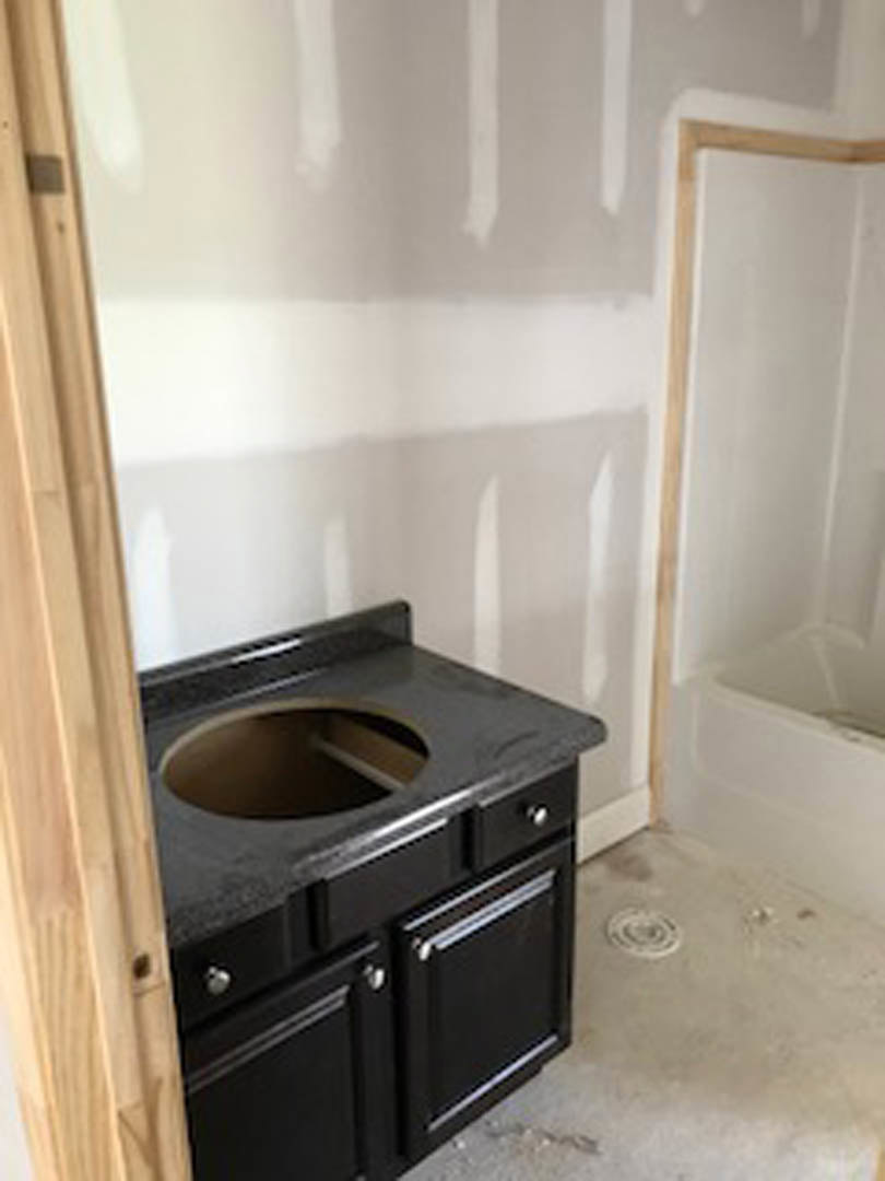 Modern bathroom featuring a freestanding white tub, black vessel sink with a round drain, light wood cabinetry, stone countertop, and neutral tile walls.