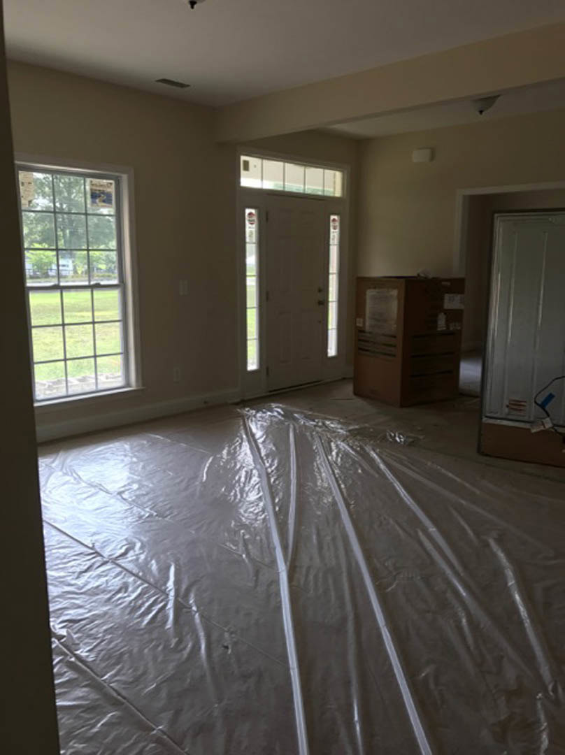 Room under construction with plastic sheeting on the floor, white door with glass panes, window with multiple square panes, brown box with white label, unfinished wall surfaces