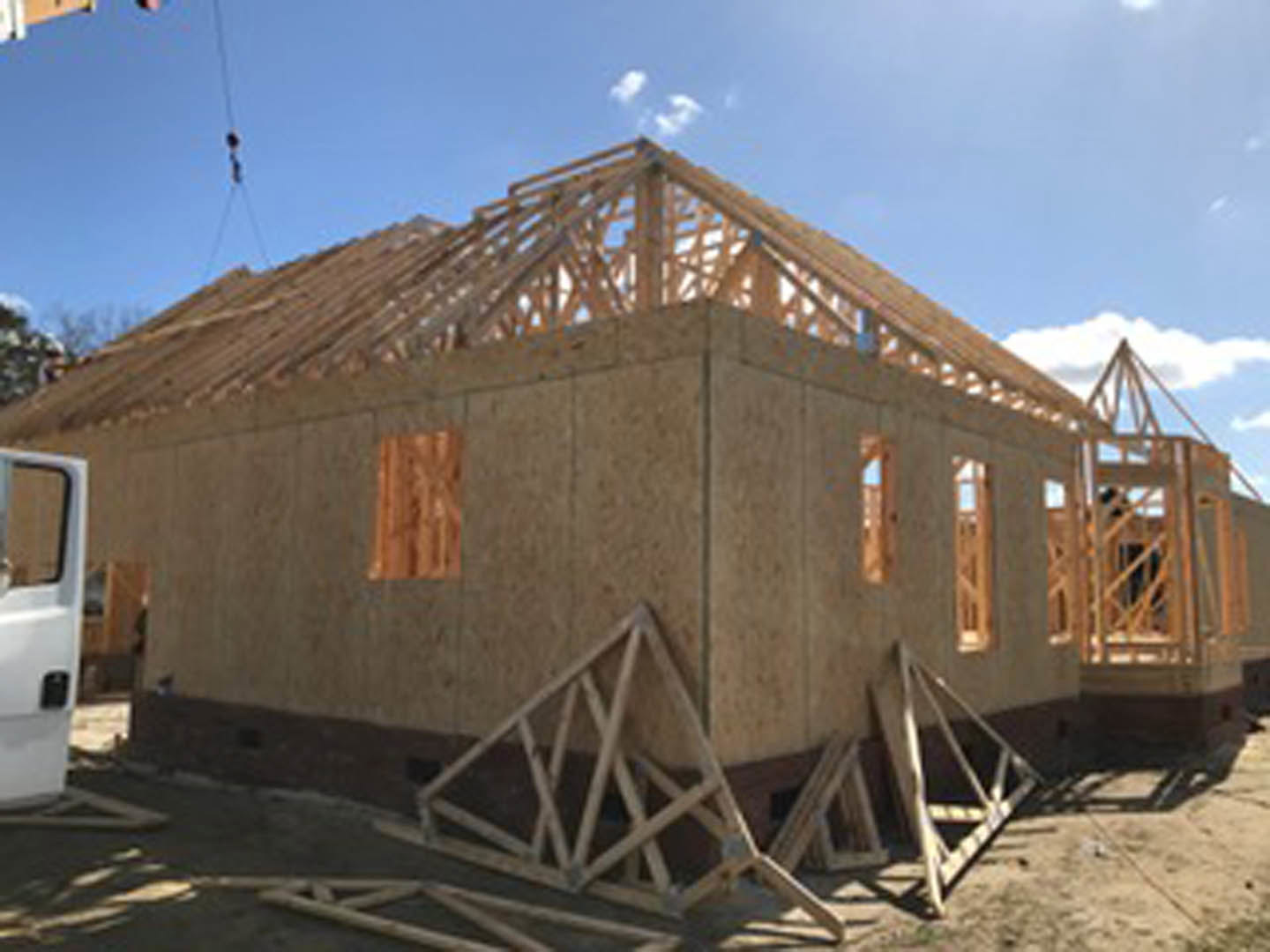 Wood-framed custom home under construction with exposed beams, crane in background, cloudy sky overhead