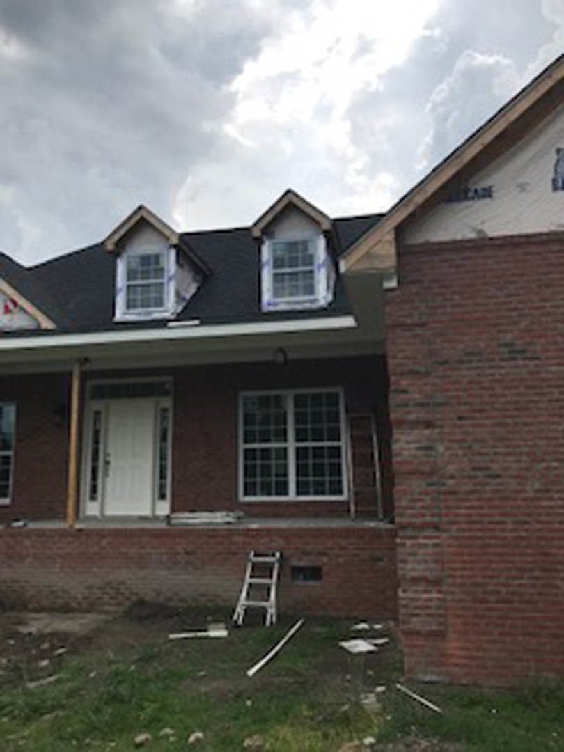 Red brick house exterior with a metal ladder leaning against the wall, multi-pane window, and white door with glass inserts under a cloudy sky