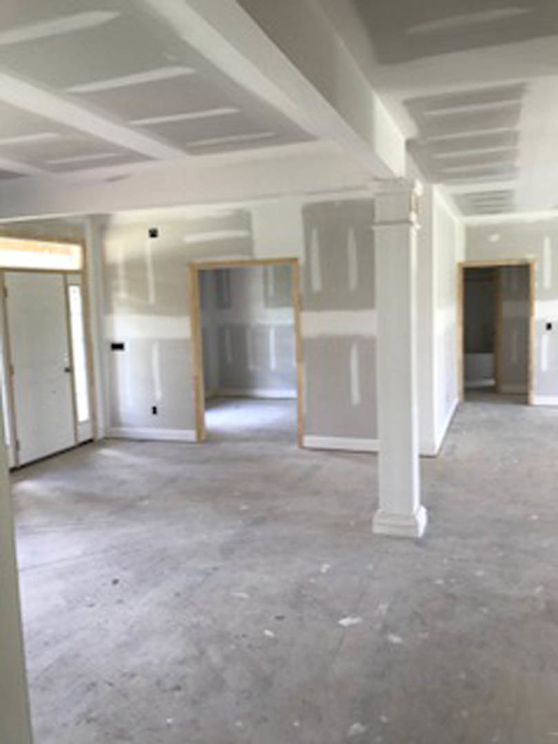 Concrete floor with white plaster columns, white walls, and a door with a black stripe.