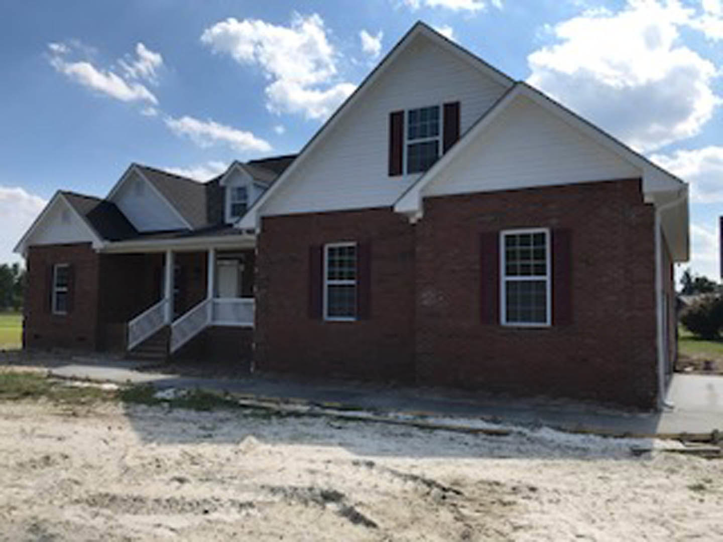 Modern cottage-style home with white metal roof, white-framed windows, light-colored exterior siding, and landscaped front yard under a partly cloudy sky