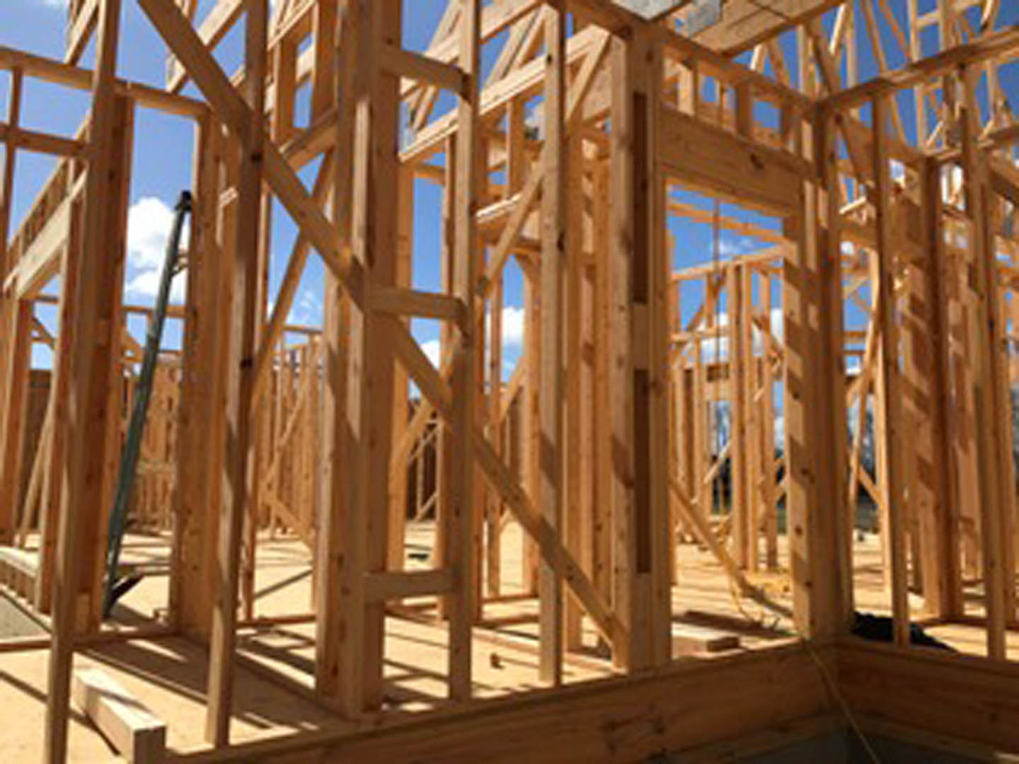 Exposed wooden beams and framing of a house under construction with clear blue sky in background