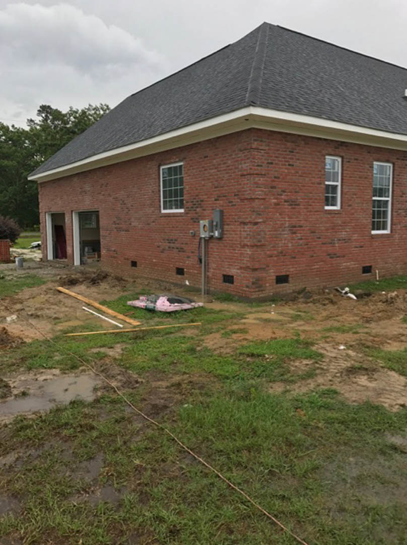 Red brick house with attached garage, grey shingle roof, multi-pane windows, grassy yard, and cloudy sky