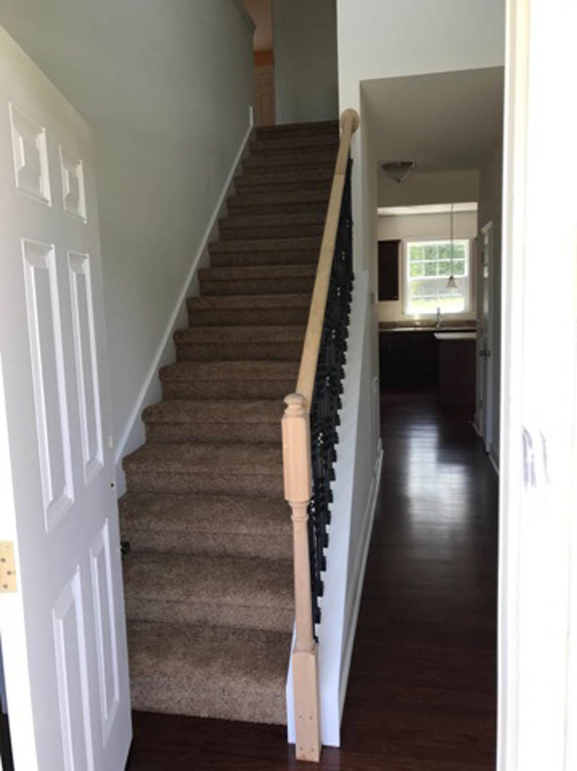 Hardwood staircase with wooden handrail and balusters, white door and window with natural light, neutral walls and flooring in residential interior