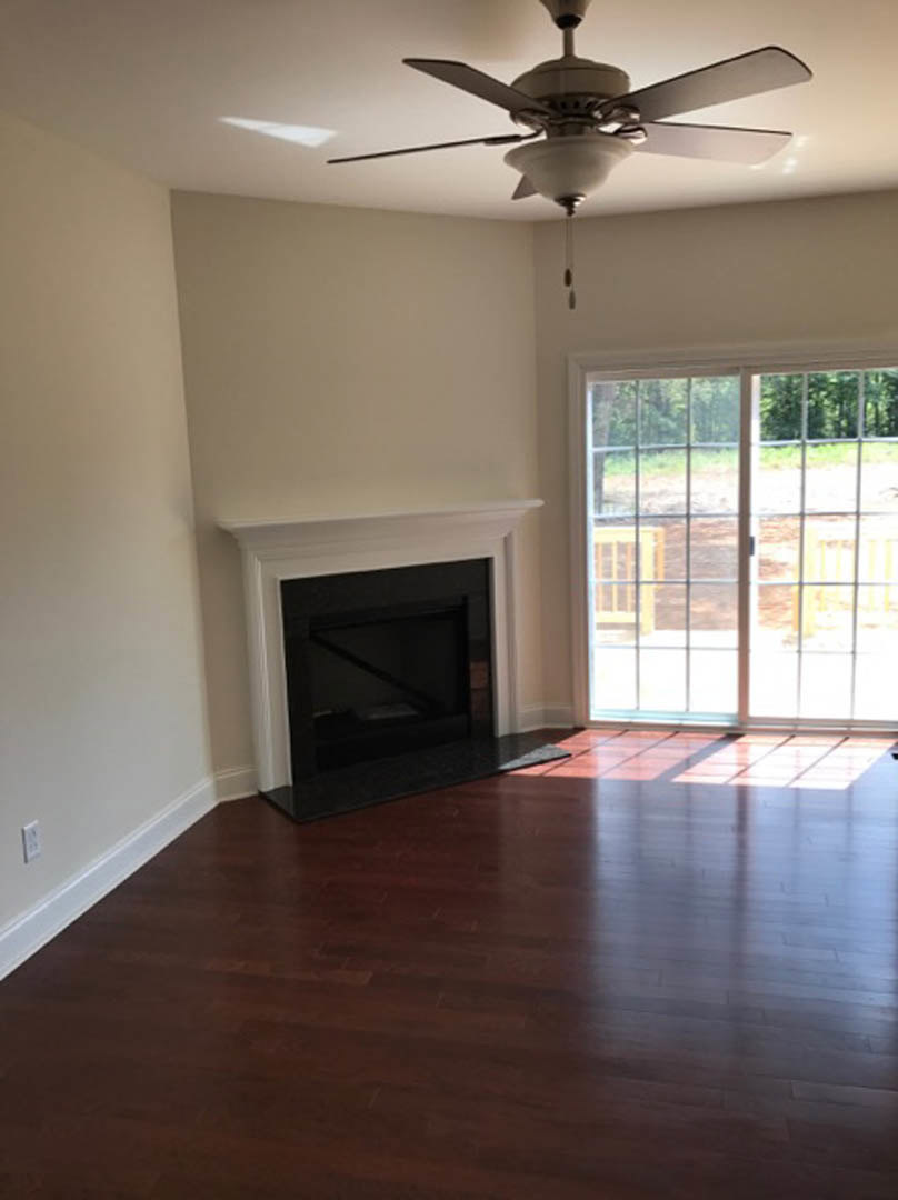 Living room with hardwood floors, black glass-door fireplace, ceiling fan with light, and glass door opening to outdoor view