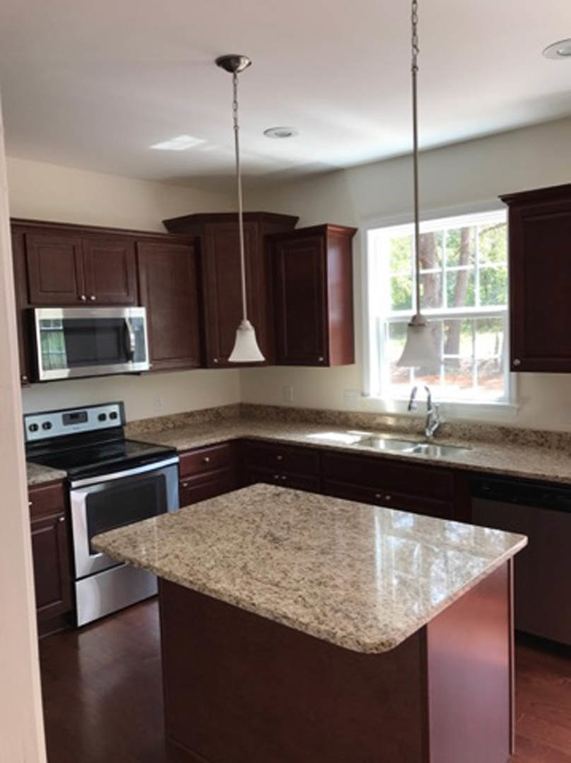 Granite countertops, dark wood cabinets, stainless steel sink, built-in microwave, and neutral tile backsplash in a modern kitchen