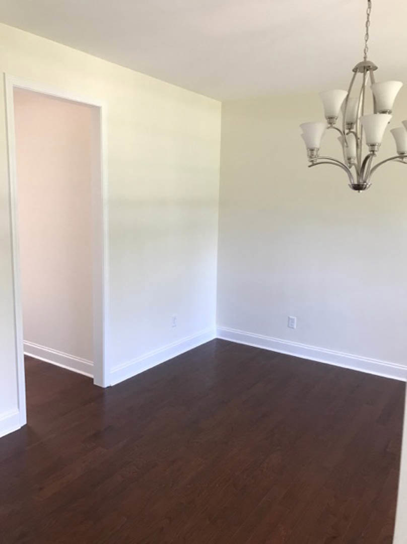 Chandelier hanging from ceiling above dark hardwood floors, white walls, and a soft pink accent wall in a residential room