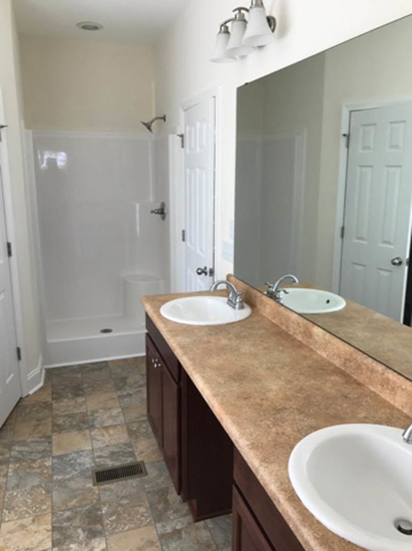 Bathroom with double sinks set in a quartz countertop, frameless glass shower with tile walls, large wall mirror, chrome faucets, and recessed lighting
