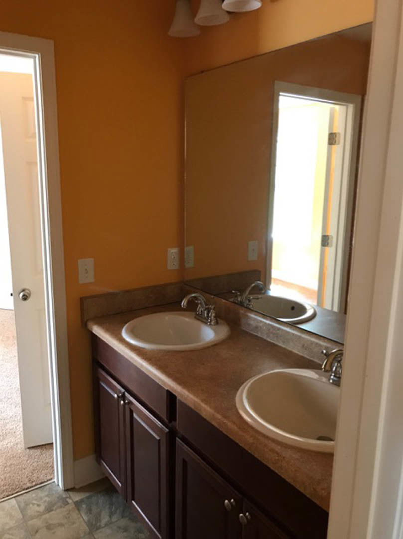 Bathroom with double vanity, quartz countertops, chrome faucets, large framed mirror, white cabinetry, and neutral tile backsplash