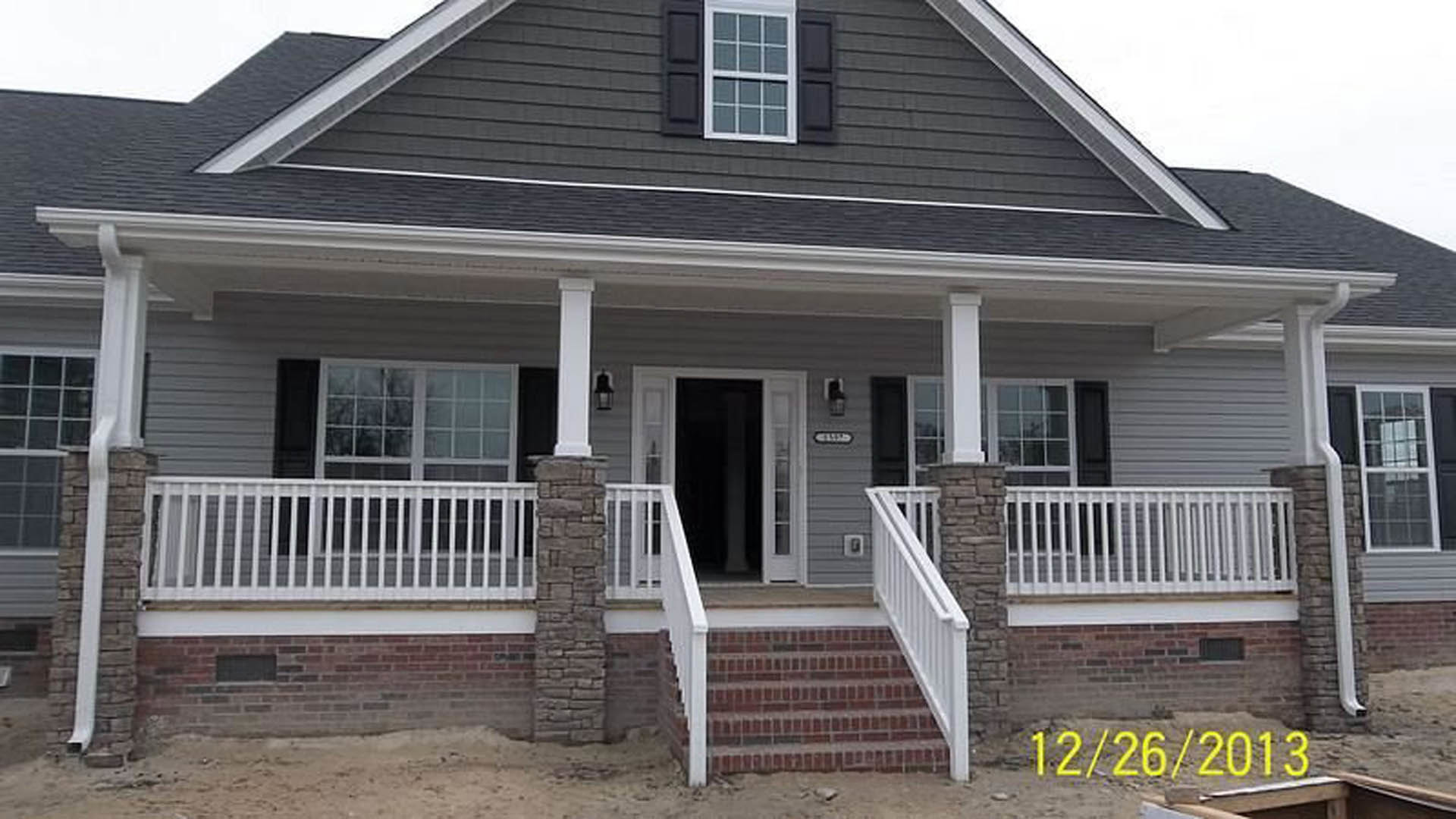 Two-story home with stone and grey siding, black front door with glass panels, double porches, white trim, yellow house numbers, and front stairs.