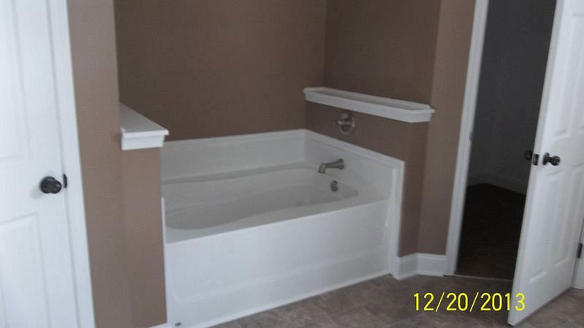 Freestanding white bathtub with chrome faucet set against light gray tiled wall in modern bathroom