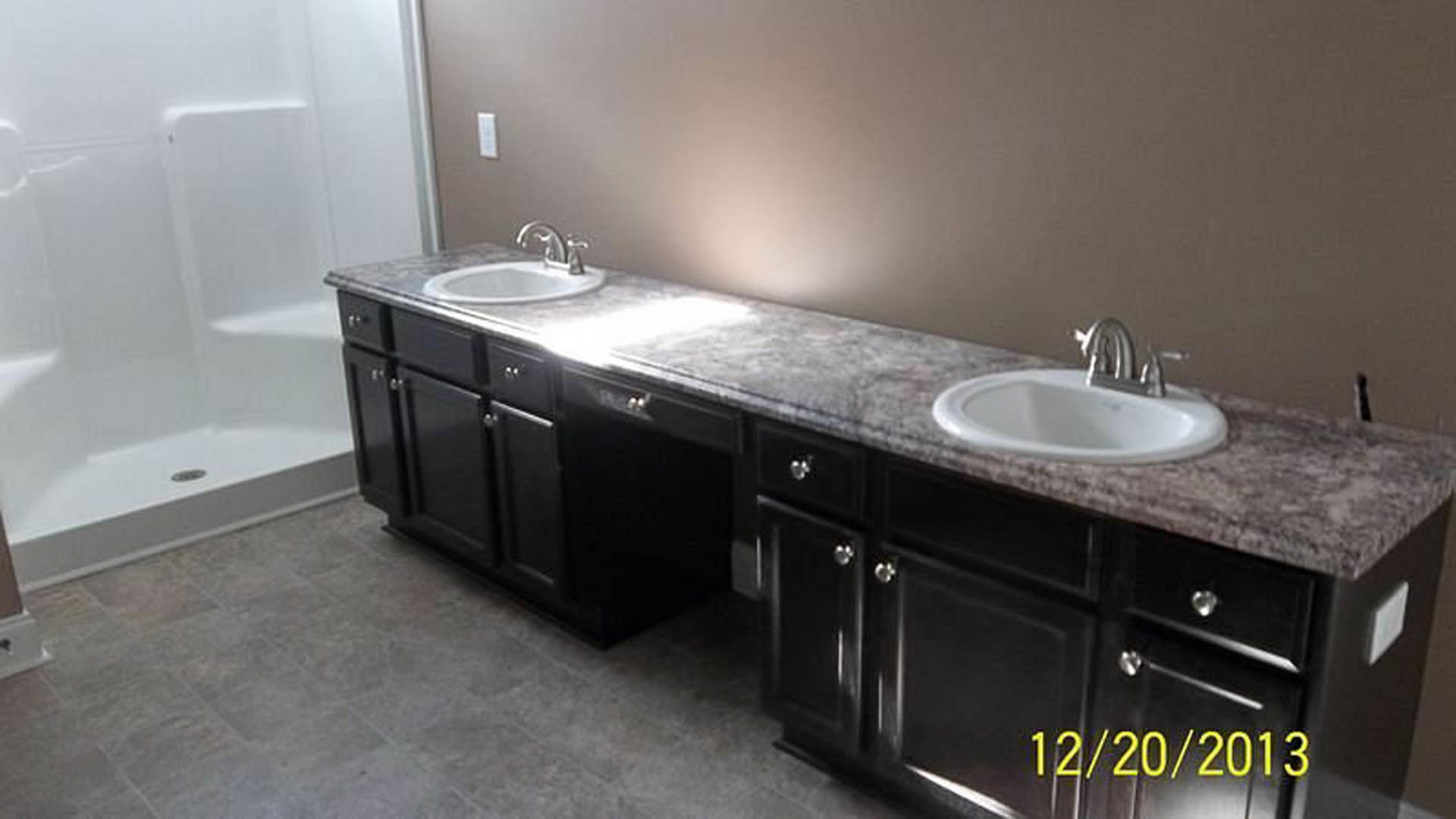 Modern bathroom featuring double white sinks set in a stone countertop, freestanding bathtub, light tile flooring, wood cabinetry, chrome faucets, and neutral wall finishes