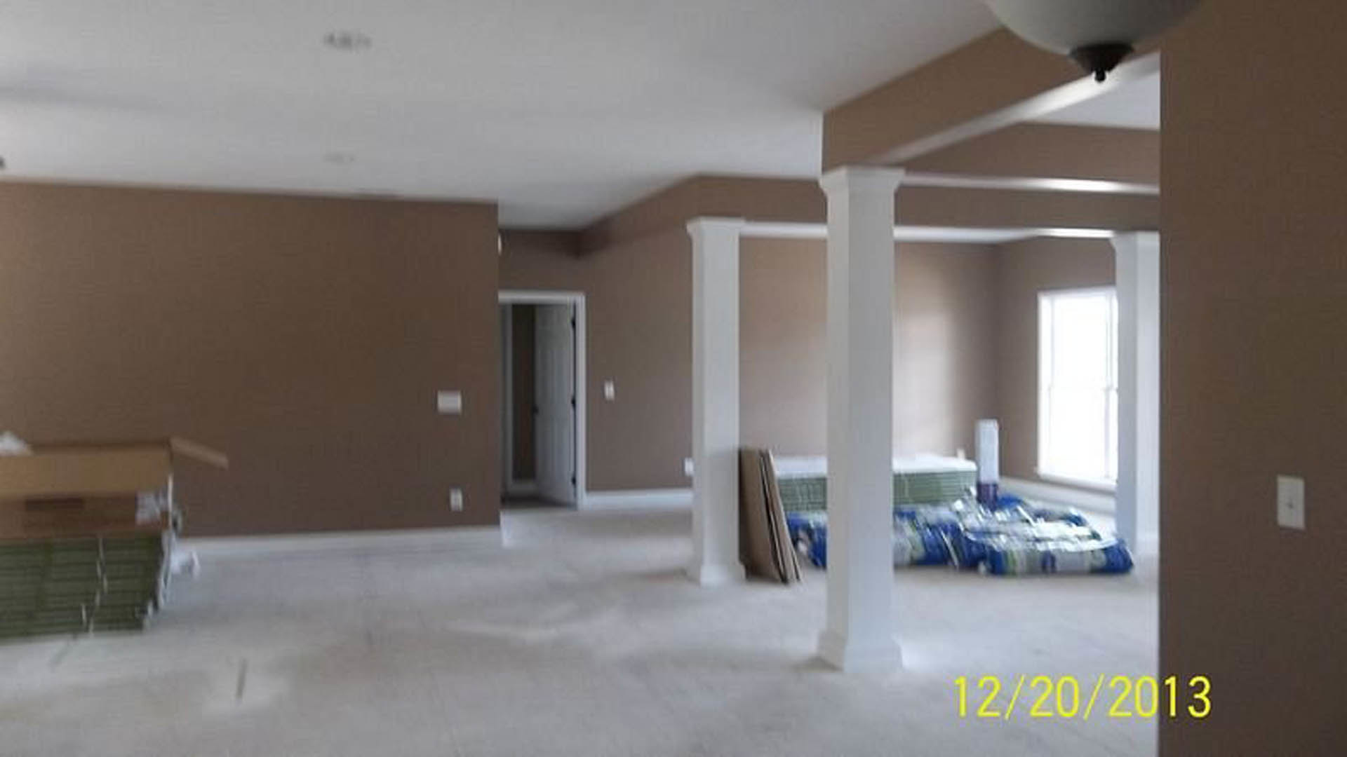 Bedroom with white square pillars, upholstered bed, light walls, and hardwood flooring