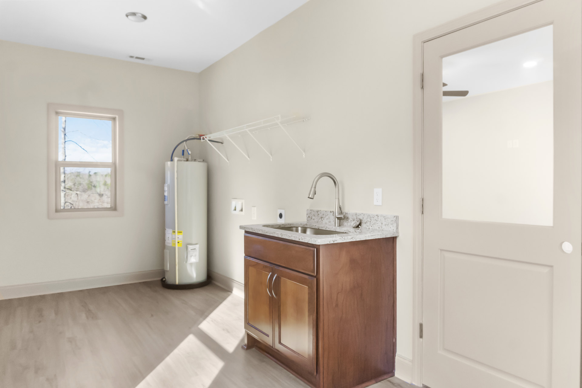 White ceramic sink with chrome faucet set in a tiled countertop, white cabinetry below, broken glass window above, white door with glass panel, and light-colored tile flooring.