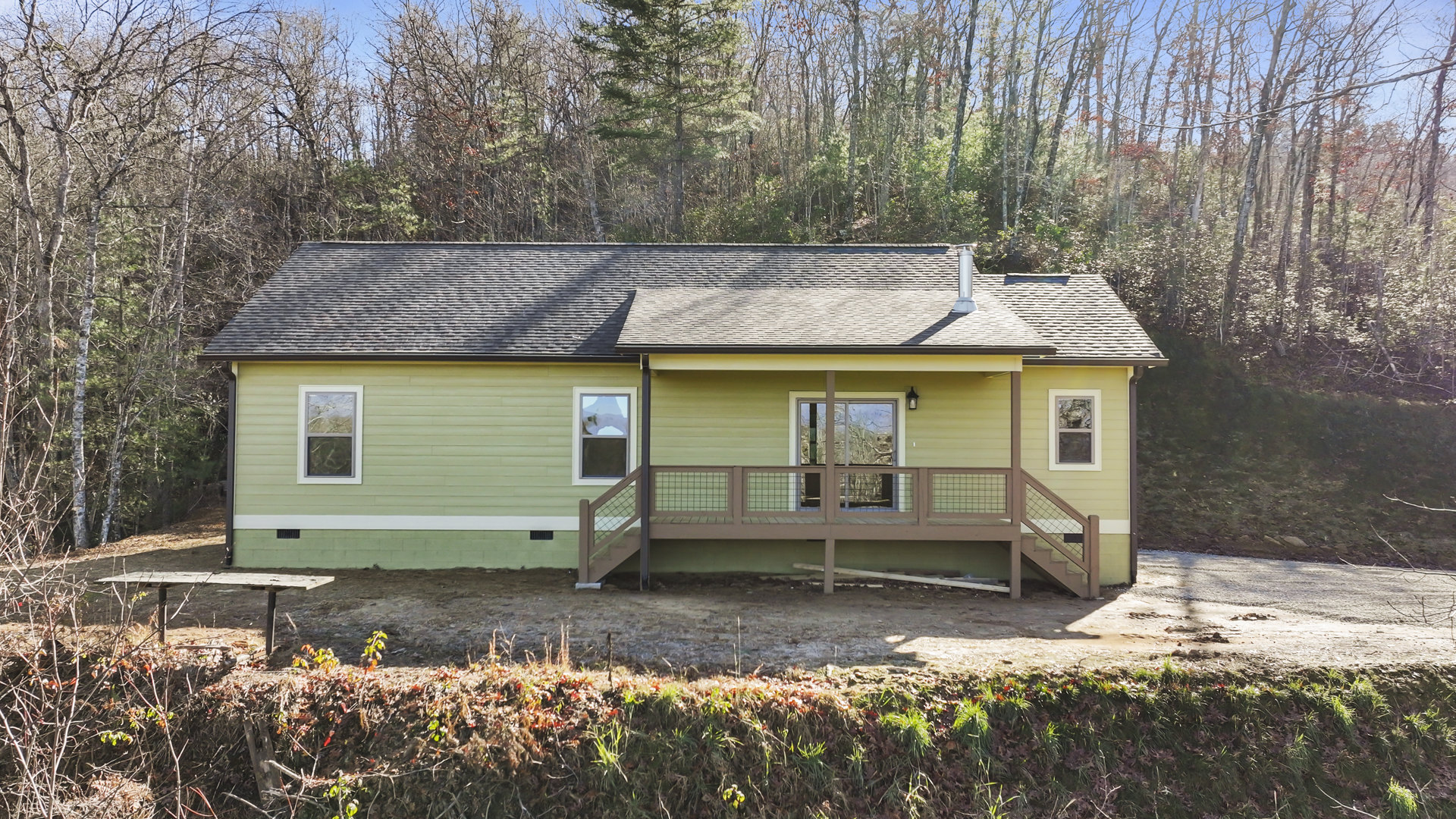 Two-story house with light siding, elevated wooden deck featuring metal railing, fenced backyard, large windows, and mature trees visible outside.