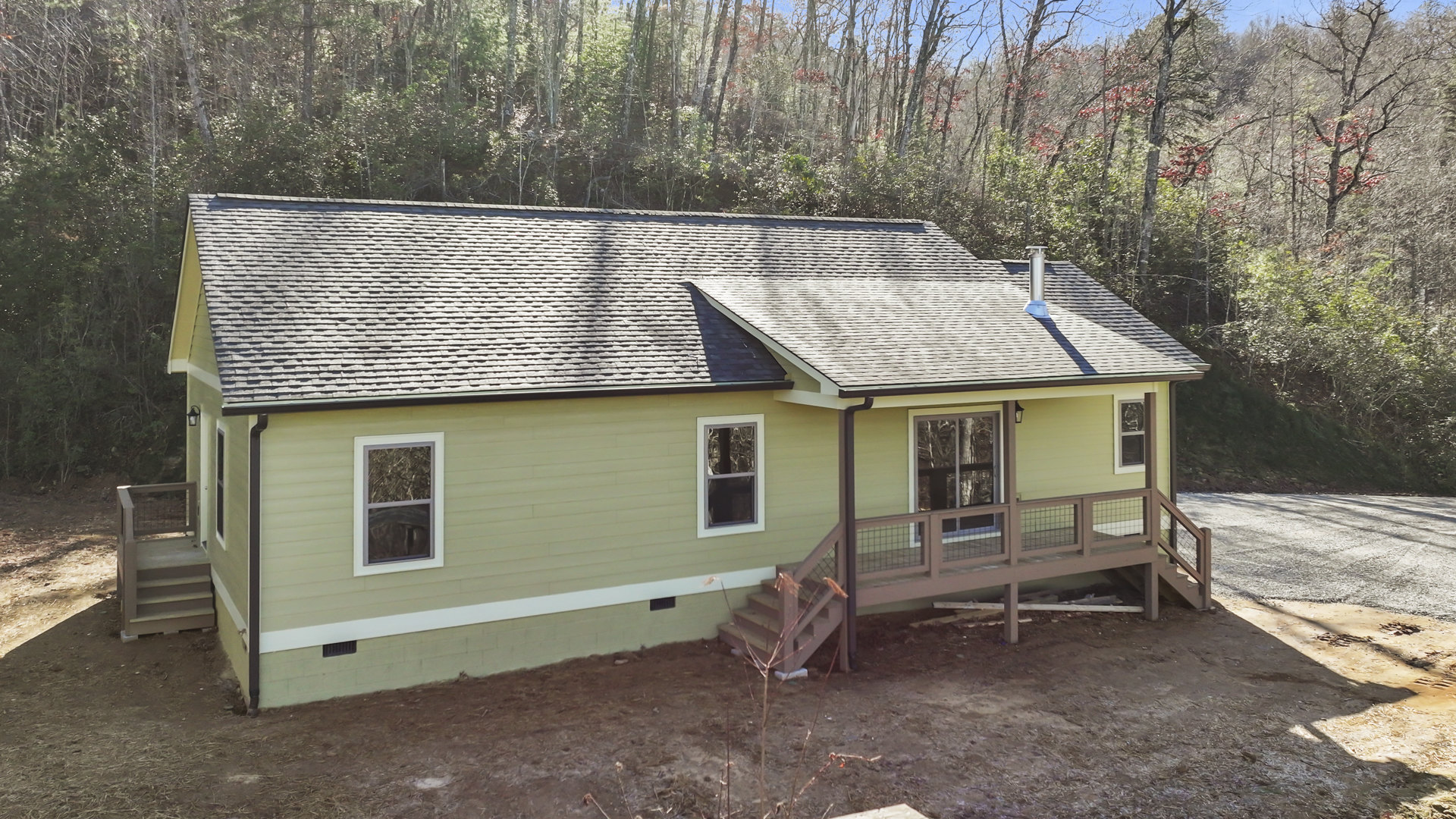 Two-story house with wooden deck and covered porch, white siding, large windows, wooden railing, stairs leading to lawn, mature tree in front yard.