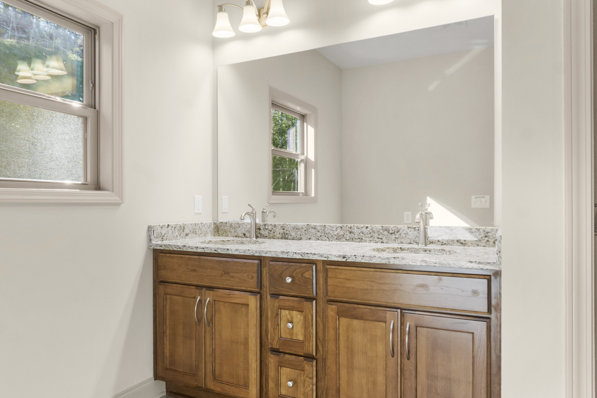 Bathroom featuring a marble countertop with an undermount sink, expansive framed mirror above, white cabinetry and drawers, modern light fixture with white shade, window with white